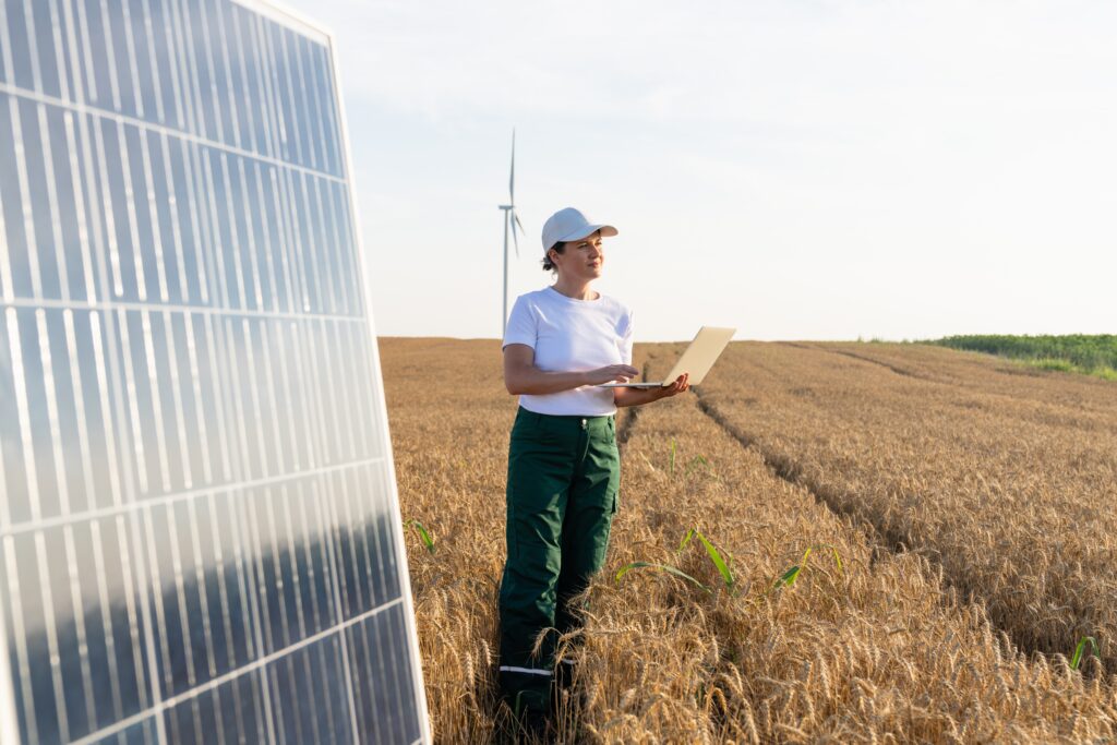 Woman with notebook standing in field in front of solar panels