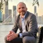 A man sitting on a chair in front of the water and a cityscape