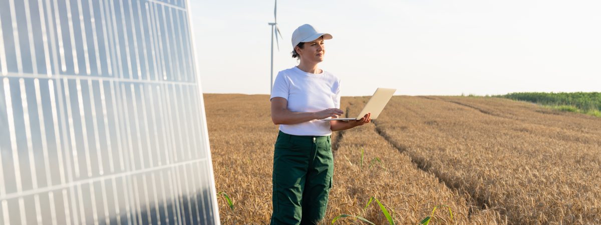 Woman with notebook standing in field in front of solar panels